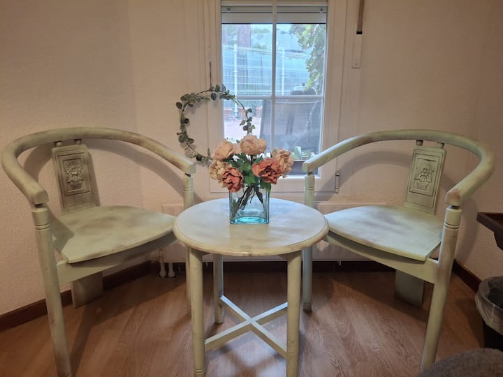 Mesita con flores y dos sillones junto a la ventana: un rincón luminoso para charlar tranquilamente.