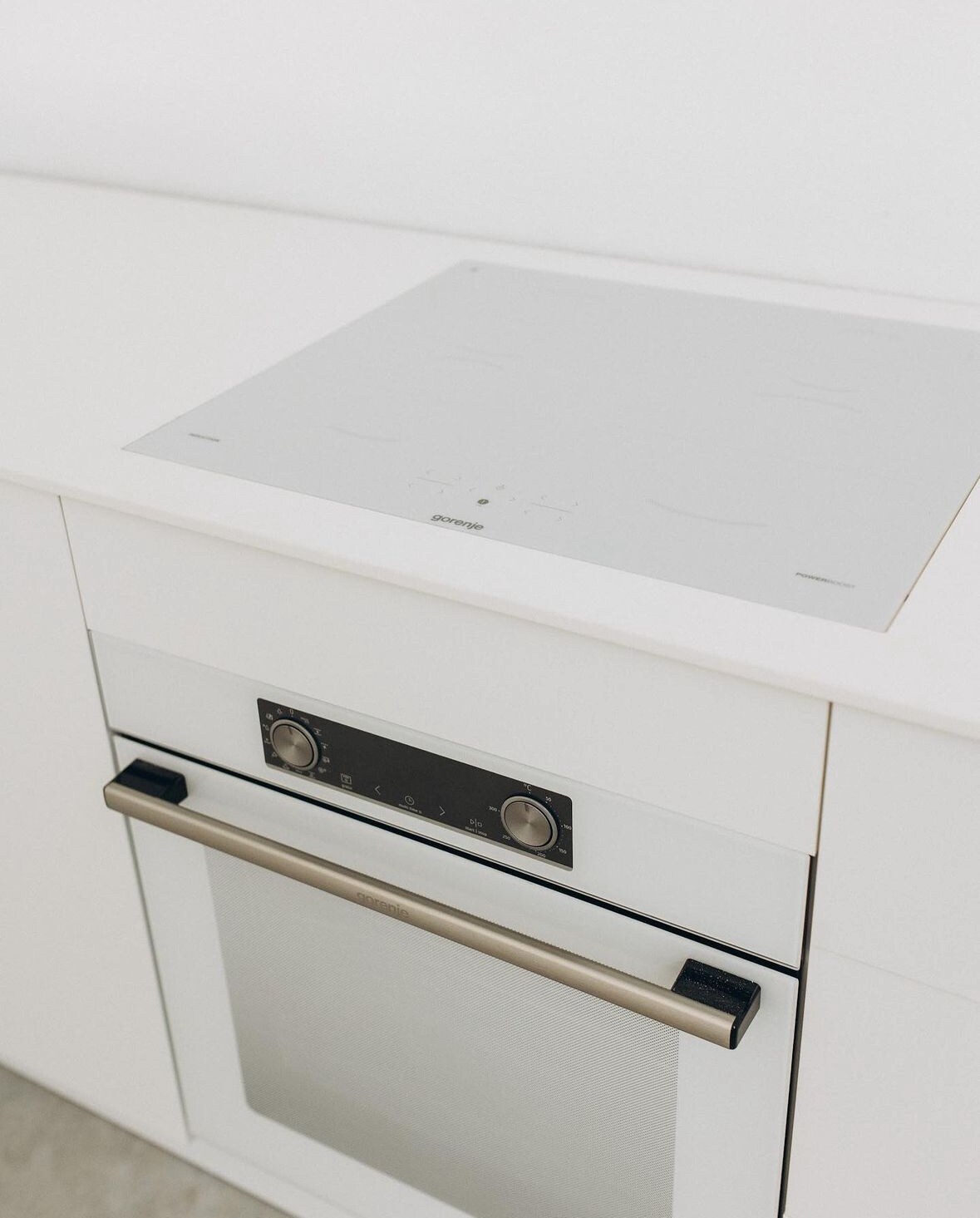 A modern kitchen area is showcased with a sleek induction cooktop and an oven integrated into the cabinetry. The surfaces are finished in a clean white, allowing the minimalist design to stand out without distractions.