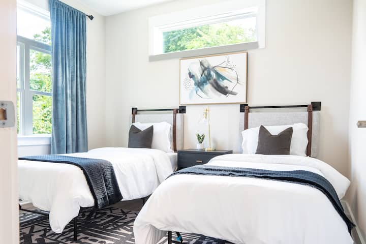 غرفة أنيقة تحتوي على سريرين متماثلين مع بياضات أنيقة وديكور متطابق وإضاءة مريحة، مثالية لمساحة مشتركة حديثة ومريحة.