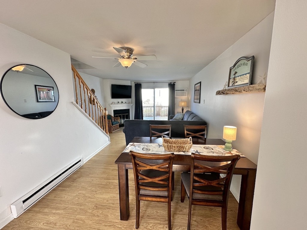 An open living area features a dining table with seating for six, complemented by a decorative centerpiece. A comfortable seating arrangement faces a wall-mounted television. Natural light floods the space through large windows, while a modern ceiling fan adds functionality.
