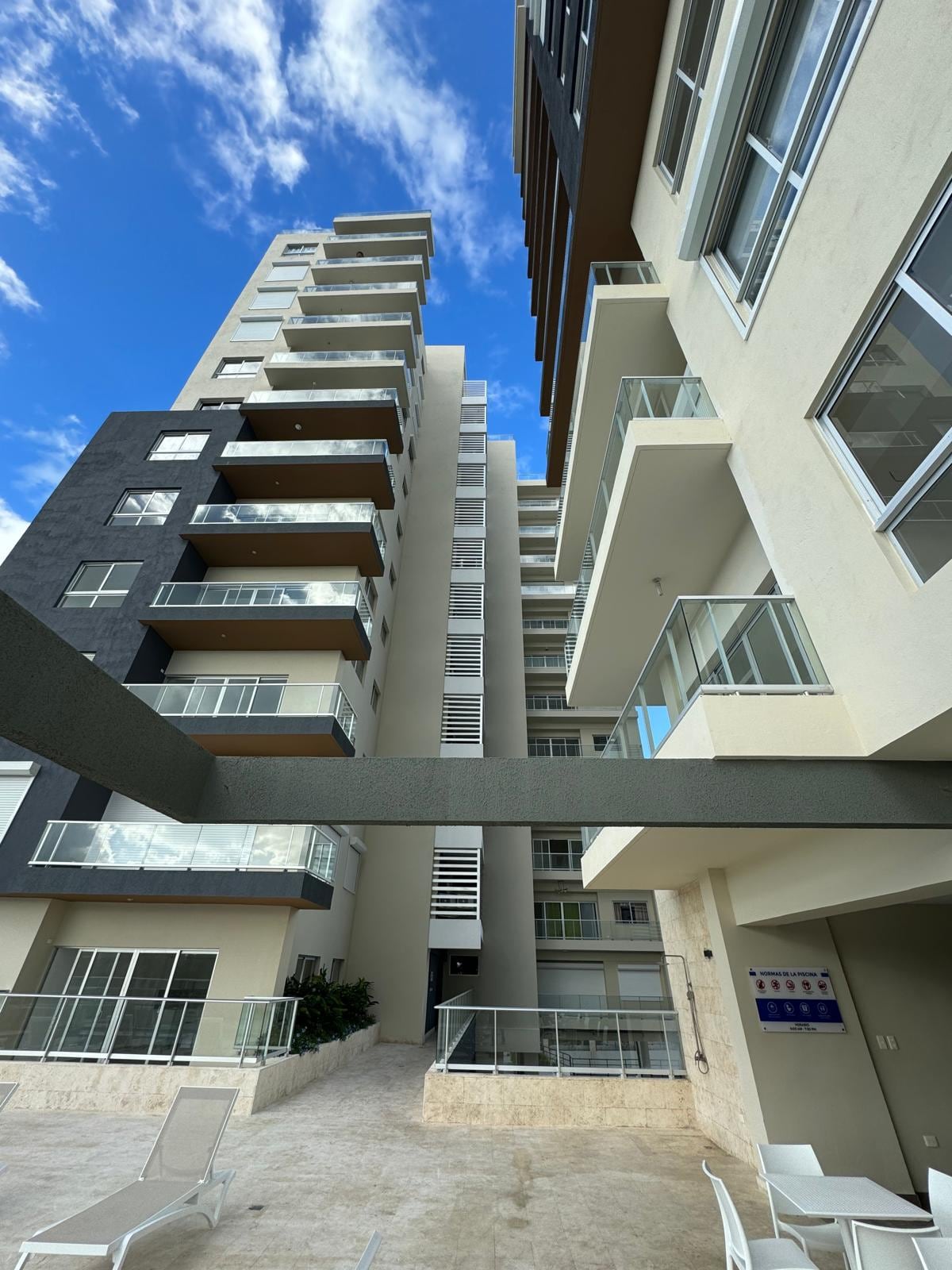The image captures the exterior of Kendasol Residences, showcasing a high-rise building against a bright blue sky. The architecture combines a modern design with large glass balconies. The surrounding area features a clean, paved space, emphasizing accessibility and the inviting community atmosphere.