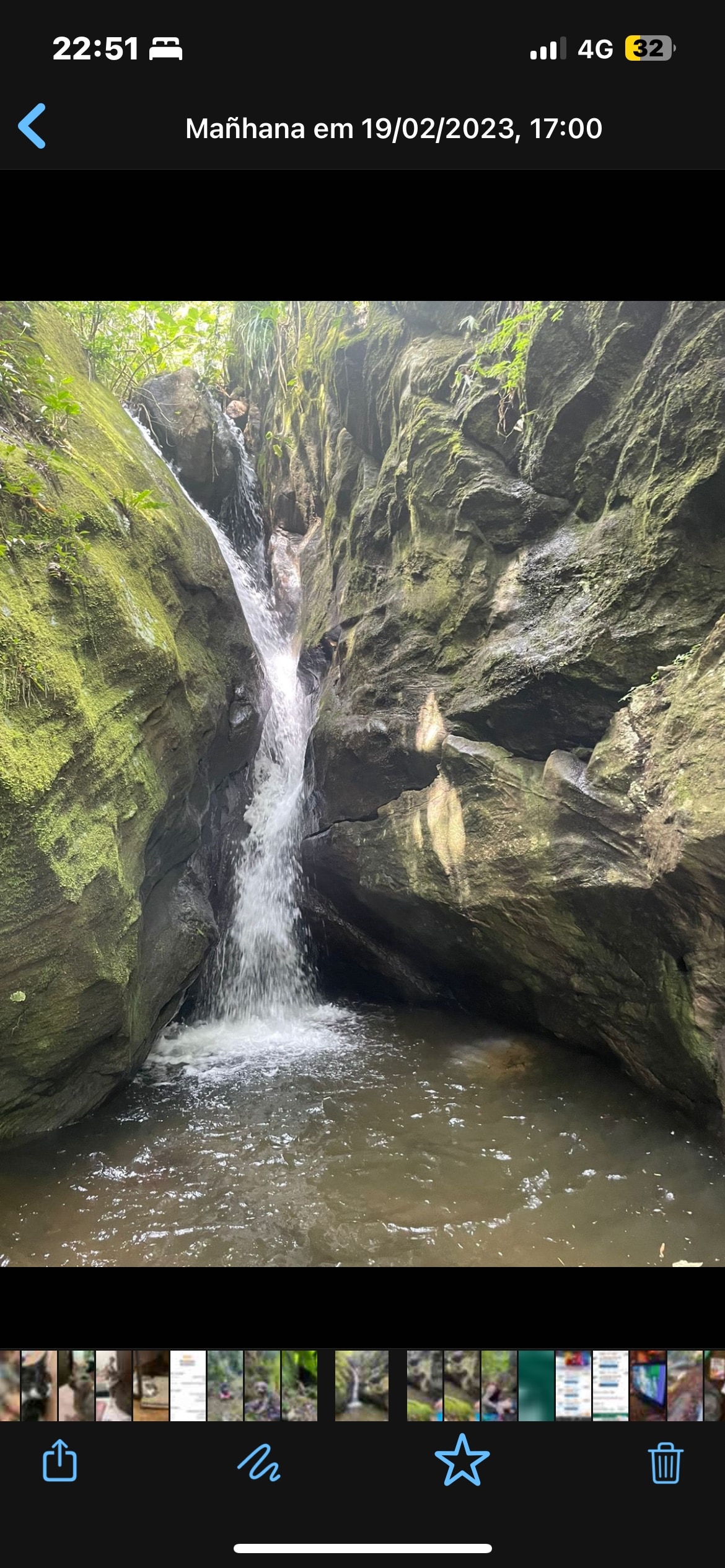 A natural rock formation is showcased, featuring a waterfall cascading down into a serene pool below. Lush greenery surrounds the area, with smooth stone surfaces contributing to the tranquil atmosphere of the scene.