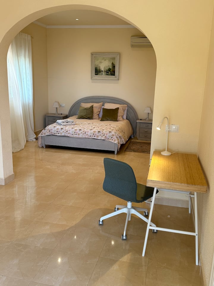 Veľká manželská posteľ s výhľadom z okna do stredomorskej záhrady.