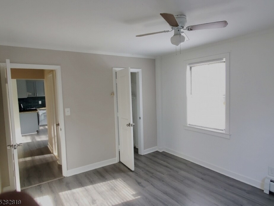 A light-filled room features a ceiling fan and is painted in soft neutral tones. Two doorways lead to adjoining spaces, while a window allows natural light to enter, illuminating the smooth flooring.