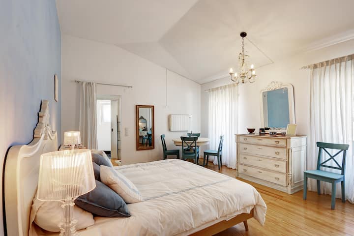 Relax in the elegant Blue Suite, featuring a comfortable king-size bed, a dressing table, and a round table with chairs perfect for morning coffee or reading. Large windows offer a breathtaking view of the surrounding farm environment