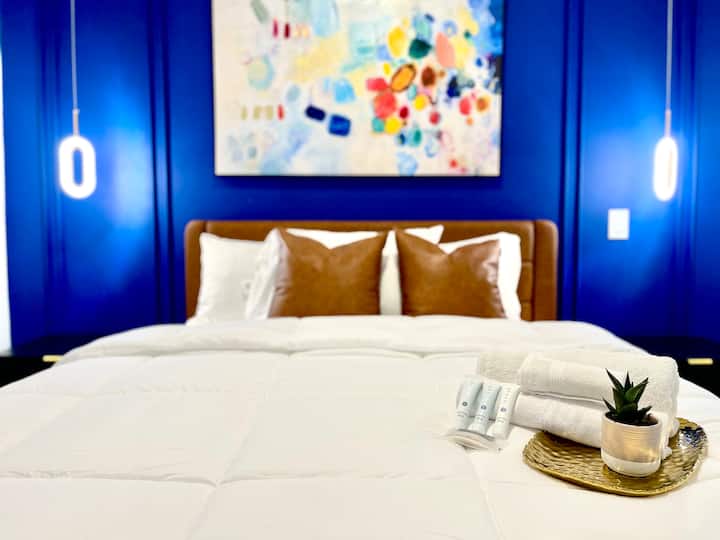 Rest easy in this vibrant room with a comfy bed, bold blue walls, and lively art that adds character and charm to your stay.