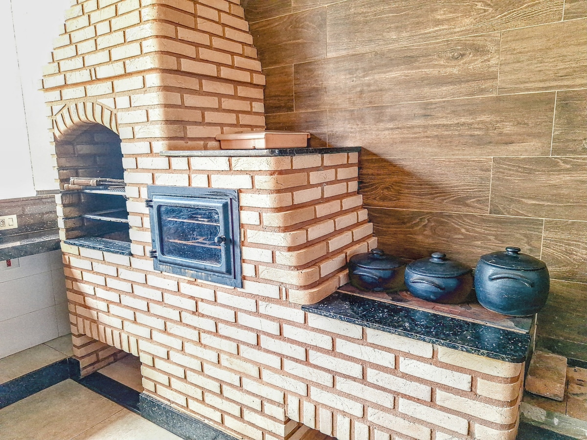 An outdoor kitchen area features a brick oven, designed for cooking, alongside a countertop made of dark granite. Several black cooking pots are positioned on the counter, highlighting the functional design of the space.