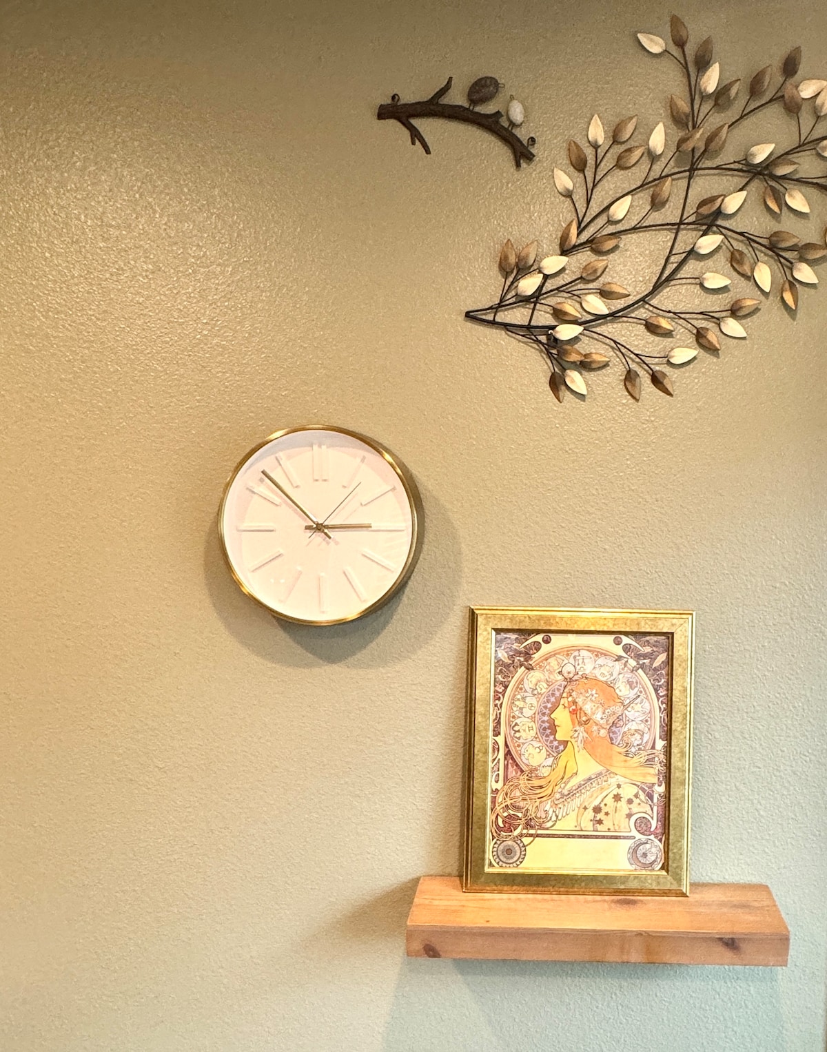 A wall features a round clock and a decorative gold-framed artwork. Above, a branch design is mounted, adding a natural touch. The color palette consists of earthy tones, providing a cozy backdrop for the items displayed.