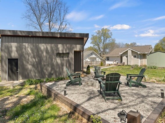 A private outdoor area features a gravel patio with multiple green Adirondack chairs arranged around a fire pit. The backyard is landscaped with gardens, and a small wooden structure is visible nearby, adding to the serene setting.