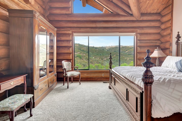 Spacious guest bedroom with stunning hillside views—king bed with elegant carved posts, vaulted ceilings with high windows, ample storage, and peaceful retreat atmosphere