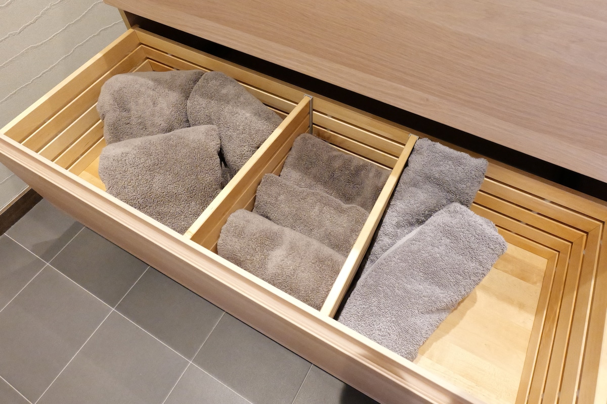 A wooden drawer displays neatly folded gray towels organized in three separate compartments. The smooth wooden base contrasts with the soft texture of the towels, creating a tidy and accessible storage space.