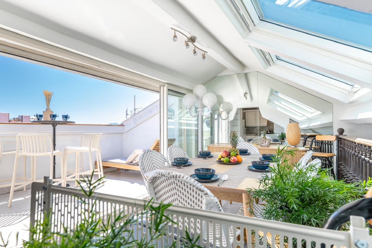A bright terrace is showcased, featuring large skylights that allow natural light to fill the space. A dining table with blue plates sits surrounded by comfortable seating. Potted greenery adds a touch of nature, while a seating area invites relaxation on sunny days.