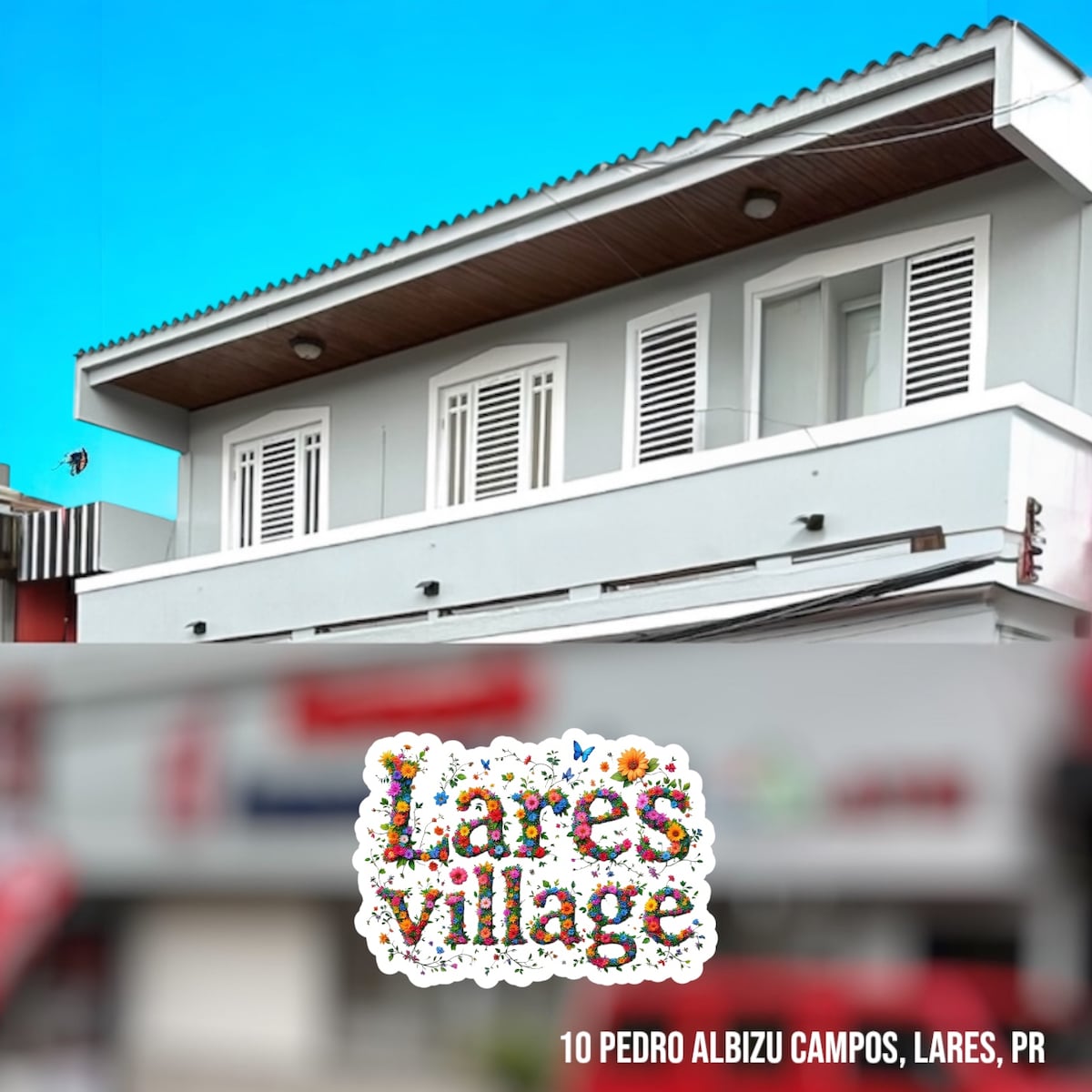 A modern building exterior is presented, showcasing a light gray facade with white shutters. The second floor is visible, featuring multiple windows that allow natural light. A sign reading 'Lares Village' is prominently displayed in colorful lettering, indicating the location.