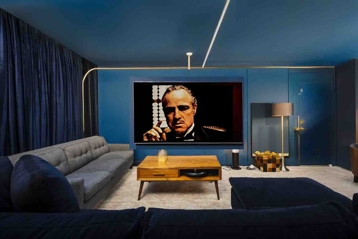 A modern living room features a spacious sectional sofa and a sleek coffee table. A large flat-screen TV dominates one wall, while decorative lighting adds a touch of elegance. Dark curtains frame the windows, creating a cozy atmosphere in the beautifully styled space.