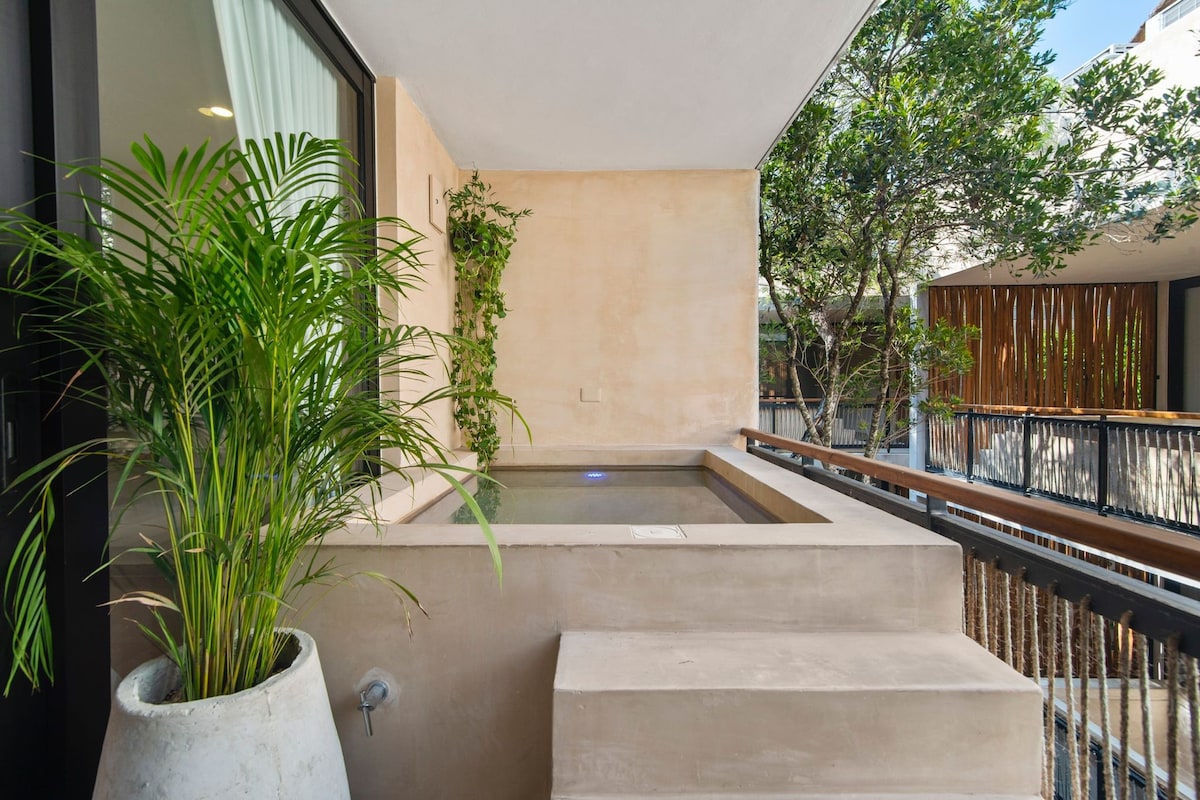 A private terrace is showcased with a relaxing plunge pool, framed by greenery. The minimalist design features smooth stone surfaces and a small set of steps leading to the pool area, creating a serene outdoor space for relaxation.