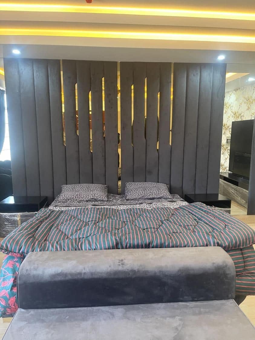 The sleeping area features a stylish headboard composed of vertical wood panels. A comforter with a striped pattern is spread across the spacious bed, while the large windows allow natural light to brighten the room.
