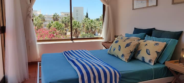 Habitación con cama de matrimonio y una hermosa vista despejada al jardín mediterráneo y a la avenida.