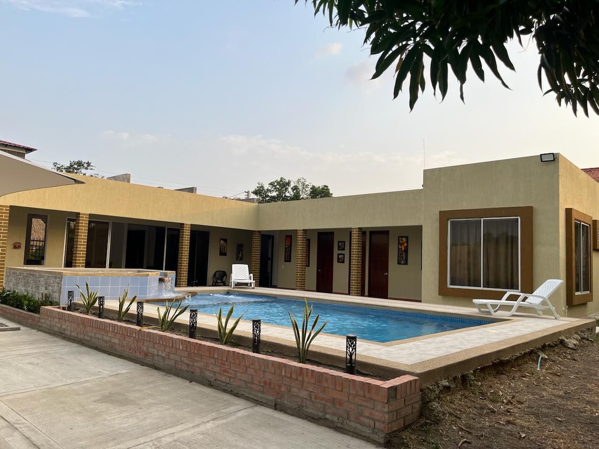 The exterior of a spacious property features a private pool surrounded by a tiled patio. Lounge chairs are positioned nearby, and the building showcases multiple doors and large windows, offering a view of the garden area with low-maintenance landscaping.