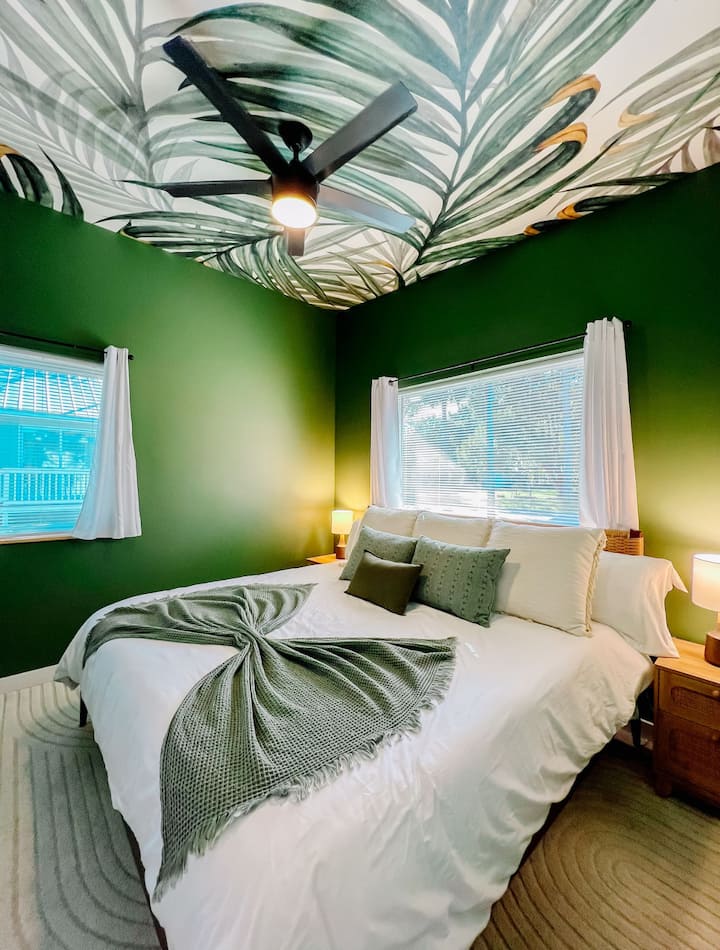 Vitajte vo svojom útočisku v džungli! Táto bujná spálňa inšpirovaná tropickým štýlom má odvážne zelené steny, zelené umelecké stropy a útulné detaily pre pokojný a nezabudnuteľný pobyt.