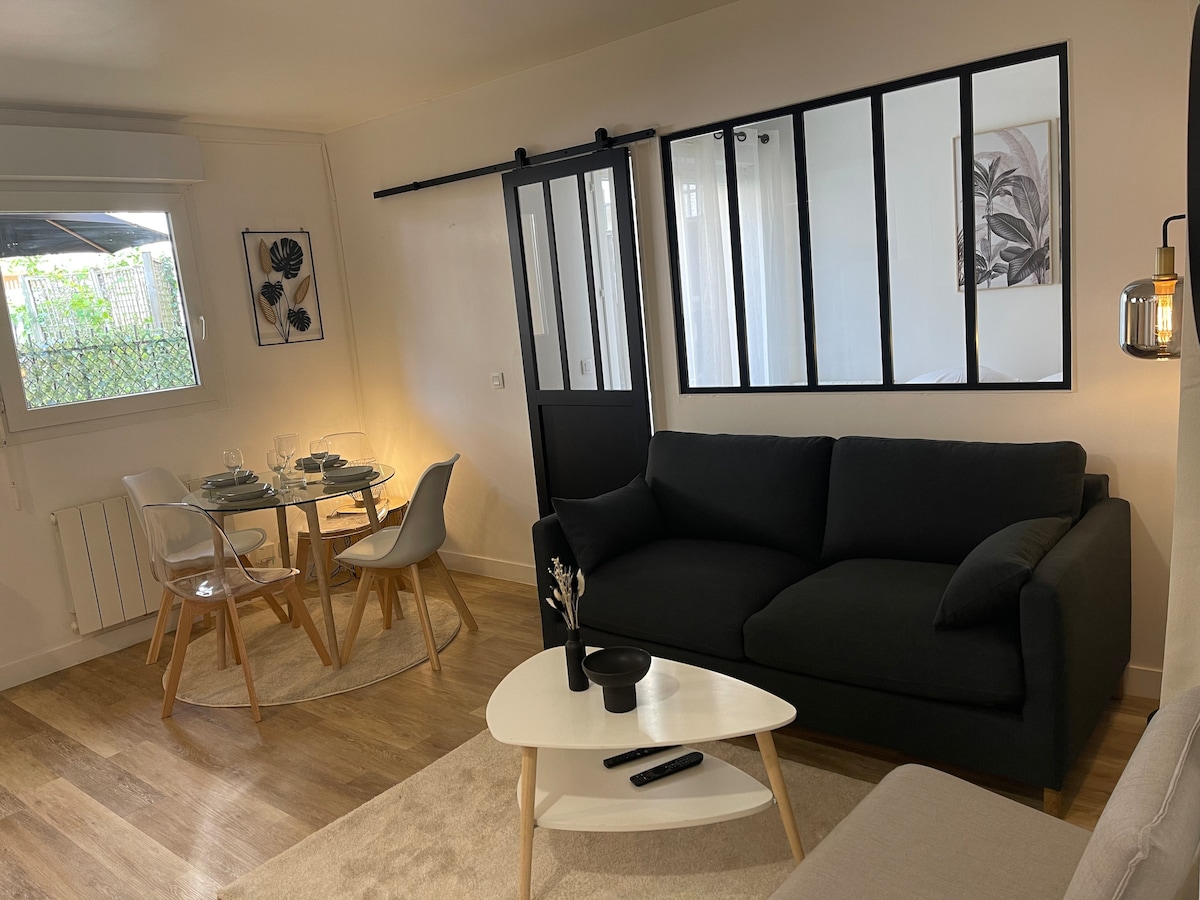 An open living space features a dark sofa paired with a light coffee table. A glass-paneled partition offers separation from the adjacent area. A round dining table is set for four, with tasteful decor enhancing the ambiance. Natural light flows in through the window.