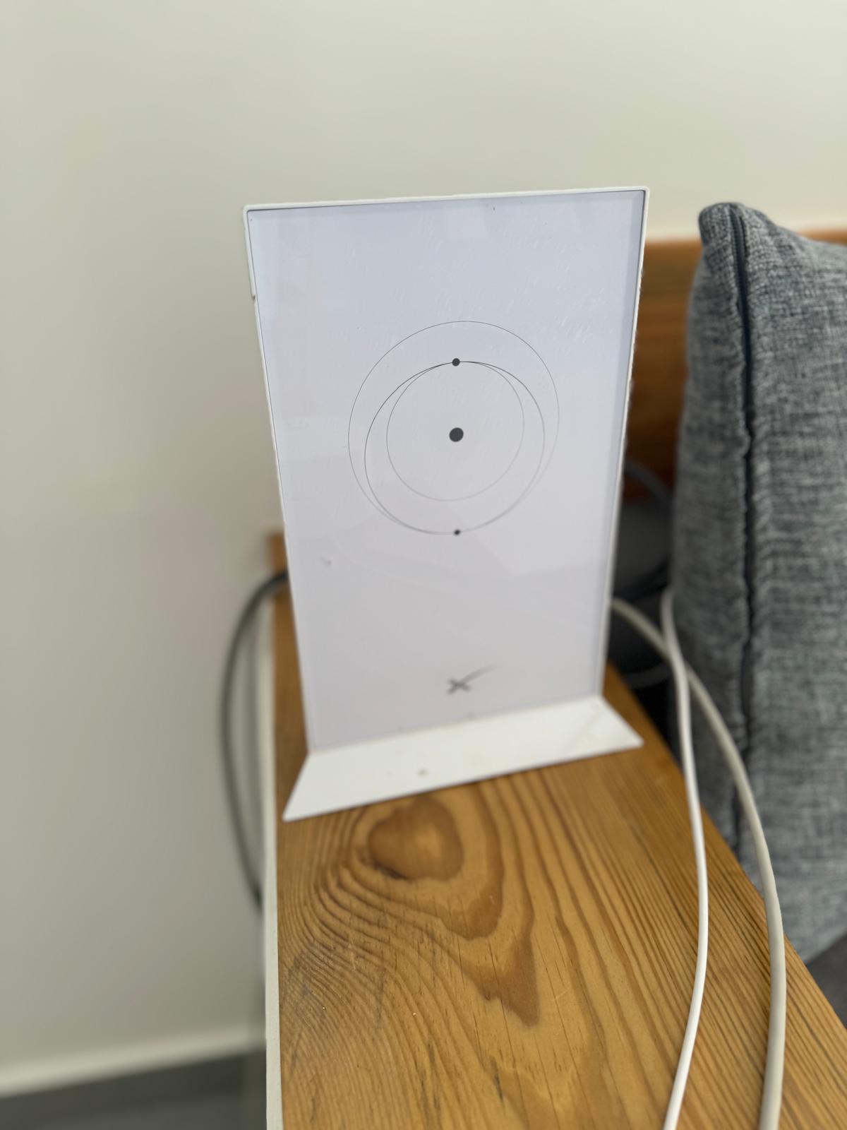 A sleek white wireless router is positioned on a wooden surface, featuring a circular design with three black dots at the center. Cables are neatly arranged at its base, contributing to a modern aesthetic.