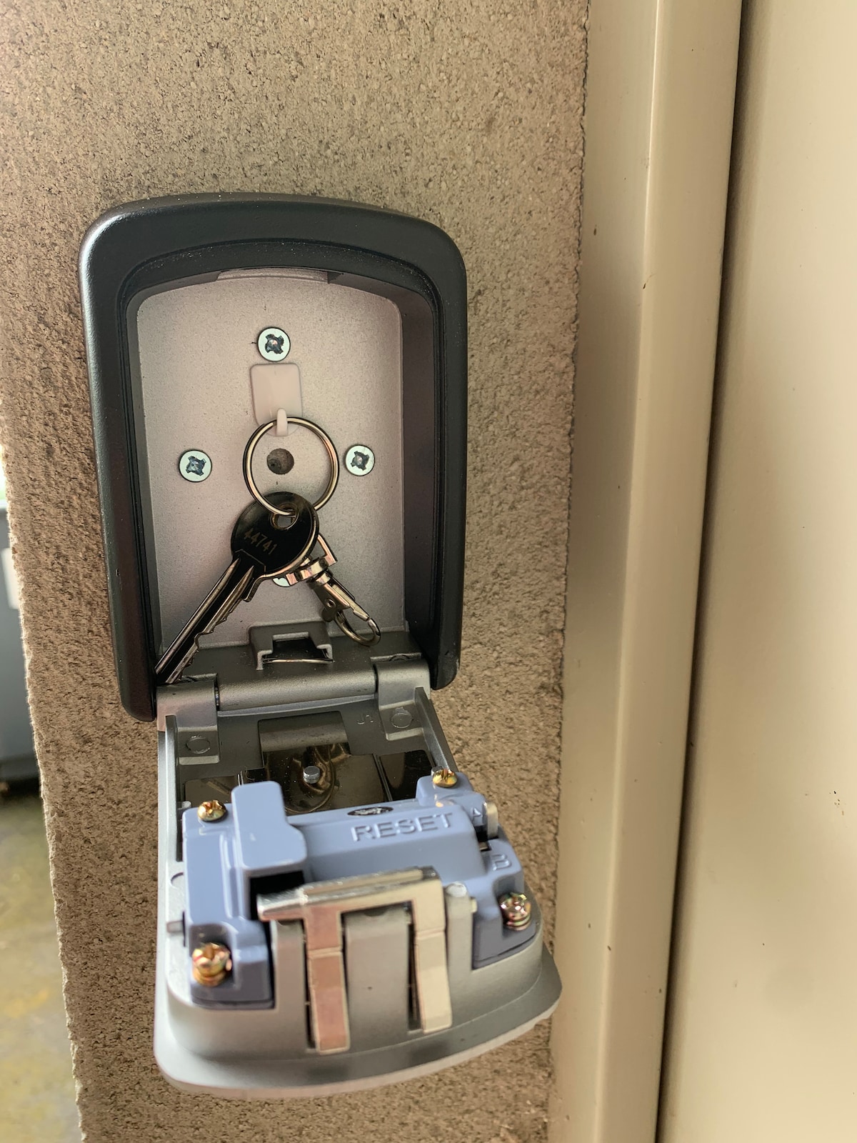 A secure combination lockbox is mounted on the wall, featuring a silver key inserted into the compartment. The lockbox has prominent brand markings and a small reset button, ensuring easy access for guests. The surrounding wall is neutral in color.