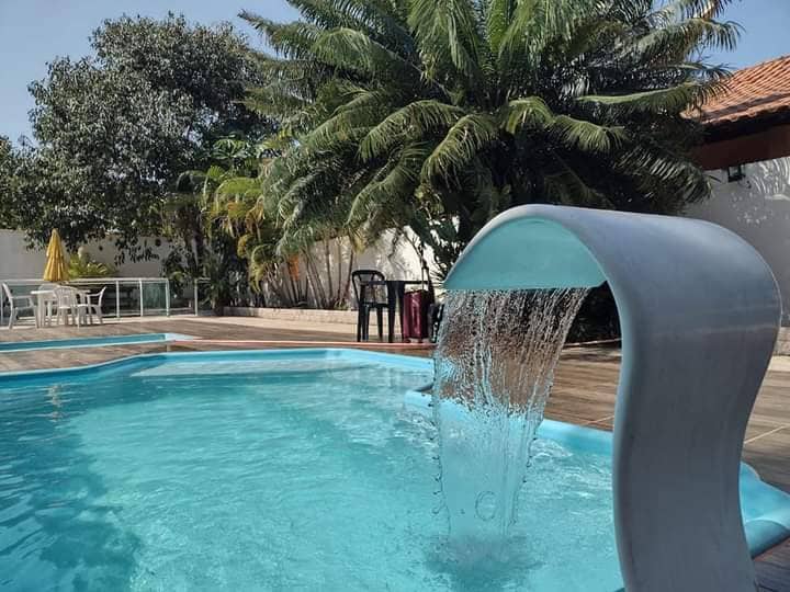 A refreshing swimming pool features a sleek water slide, with water cascading gracefully into the turquoise water. Lush palm trees and greenery provide shade, while a seating area with chairs is situated nearby, enhancing the outdoor space.