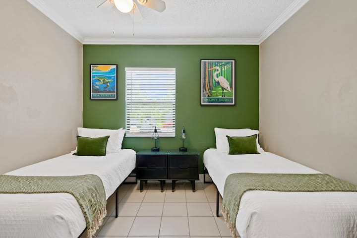Two twin beds anchor this nature-inspired room with a deep green accent wall, solid wood bedside tables, & USB-equipped lamps. Park posters of a Snowy Egret & sea turtle reflect the wildlife you can spot at the local Johnson State Park.