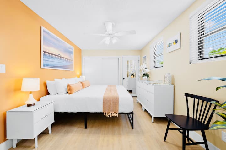 A serene master bedroom inspired by Florida piers, featuring a king-size bed, solid wood bedside tables and dressers, a large closet, a full-length mirror, and two chairs, thoughtfully designed for comfort, space, & easy, relaxed living.