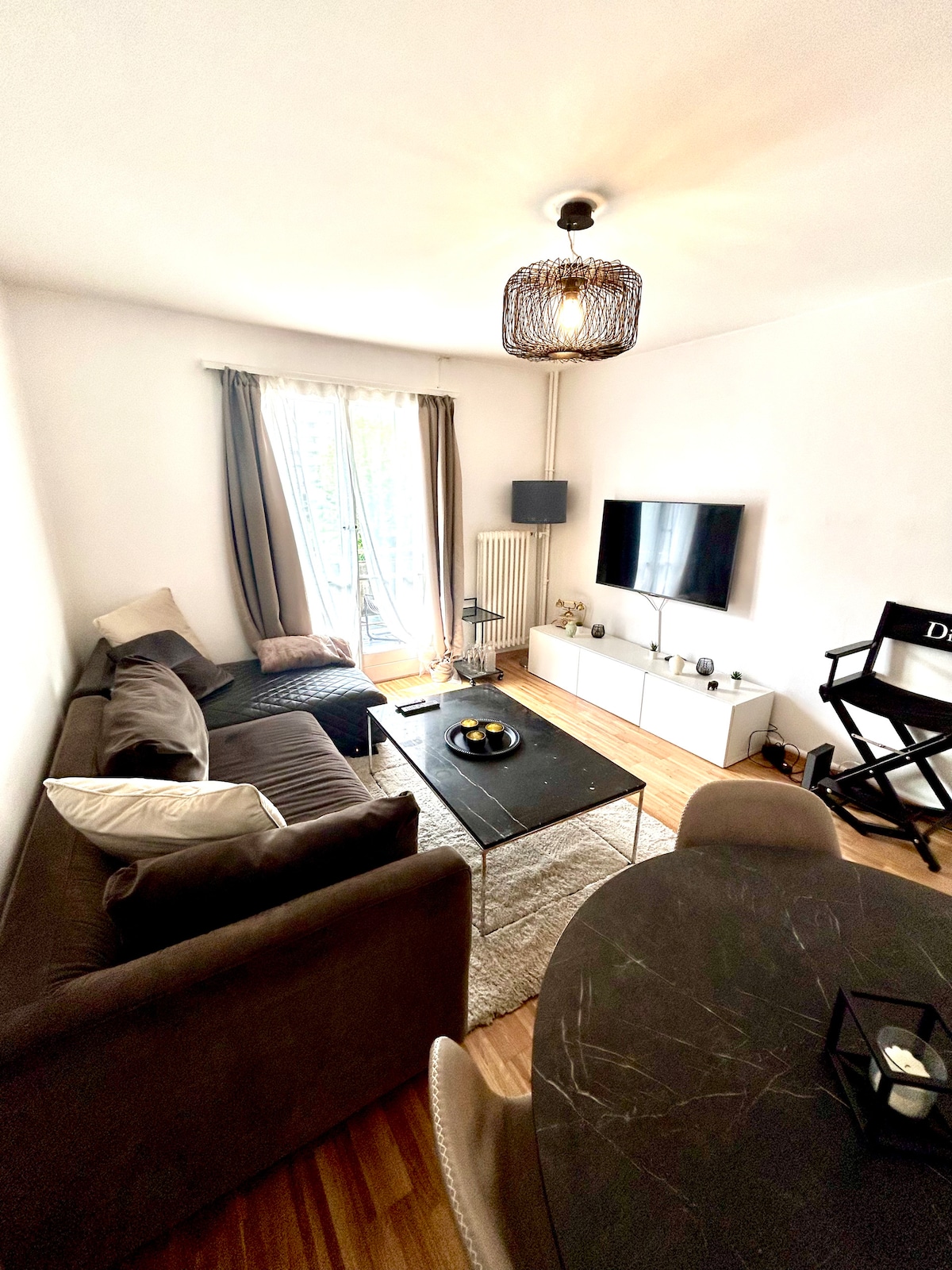 A comfortably furnished living area is featured, showcasing a dark coffee table at the center. Two sofas are arranged to facilitate conversation, while a flat-screen TV is mounted on the wall. Natural light fills the space through large glass doors leading to a balcony.