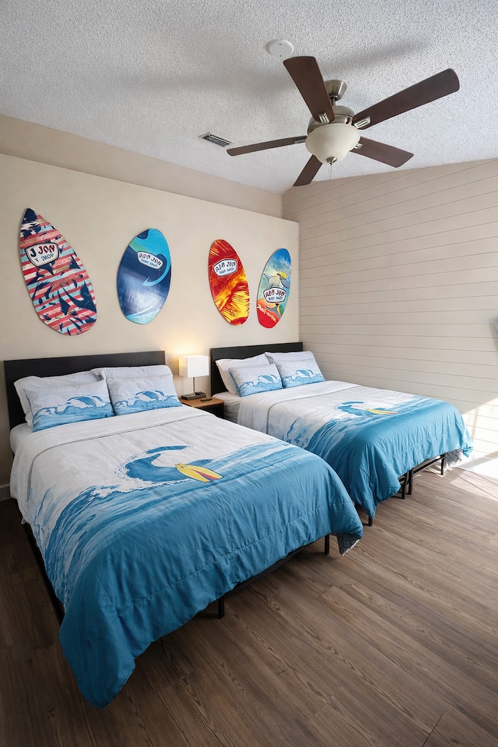 Surf themed bedroom with two comfortable beds and fun surfboard wall art that captures the laid-back Florida beach vibe.