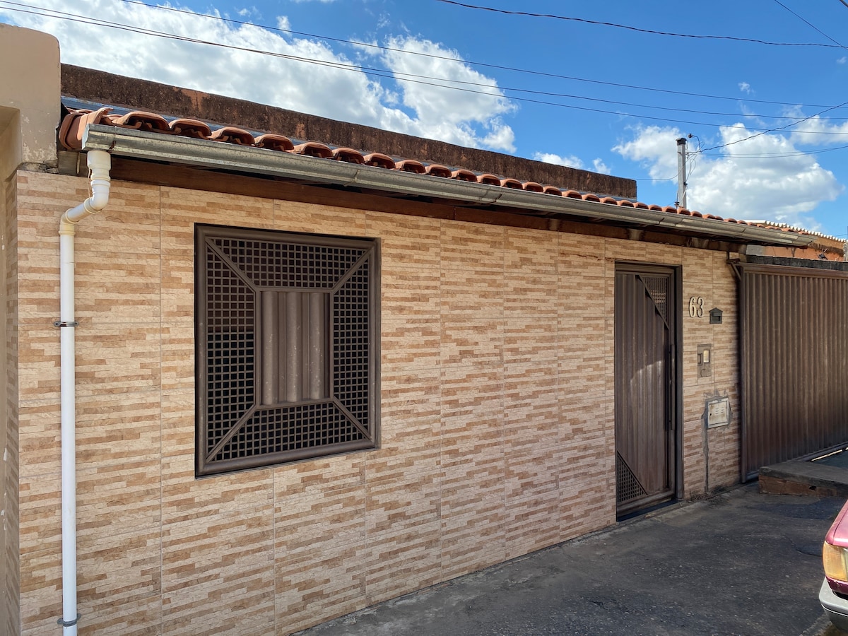 The house exterior showcases a textured stone façade with a decorative window pattern. A wooden door adds a natural element to the entrance. The roof is covered with red tiles, and the front area is surrounded by a concrete driveway.