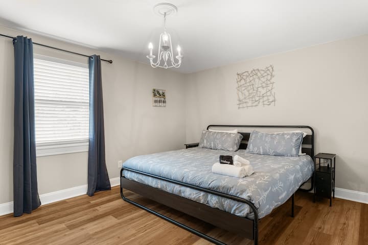 Letto matrimoniale grande con portavaligie e tende oscuranti per la stanza.  La biancheria da letto include un materasso in memory foam e lenzuola bianche in 100% cotone.  I tavolini sono dotati di caricabatterie USB.