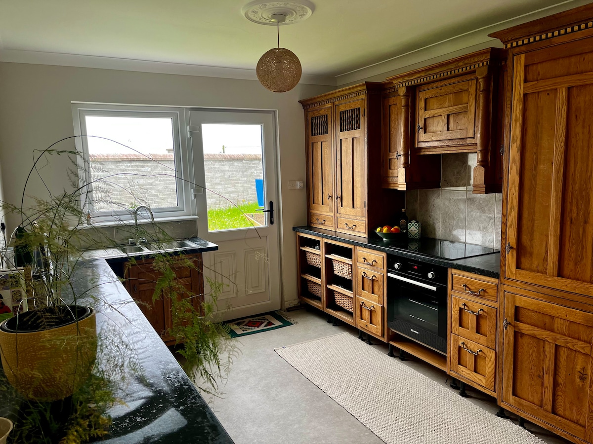 A well-equipped kitchen features wooden cabinetry with a classic design. A dark countertop contrasts with the lighter stone backsplash. Natural light floods in from a large window, highlighting an inviting arrangement of fruit. A woven rug lies beneath a small dining area.