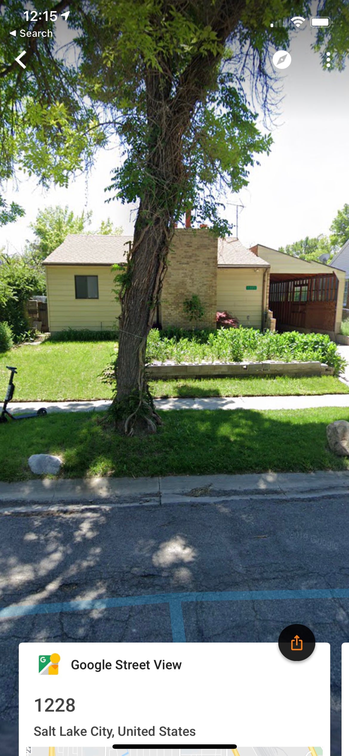 A charming house is set back from the street, surrounded by a well-maintained lawn and colorful flower beds. A large tree provides shade in the front yard, and a peaceful pathway leads to the entrance, while a driveway is visible on the side.