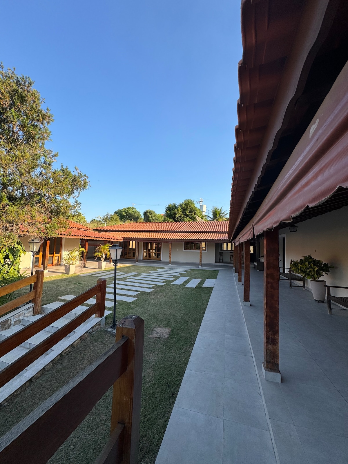 The view captures a serene outdoor space flanked by a pathway of large stones on a grassy area. Two structures with terracotta roofs are visible, surrounded by landscaped gardens, adding to the tranquil atmosphere of the property.