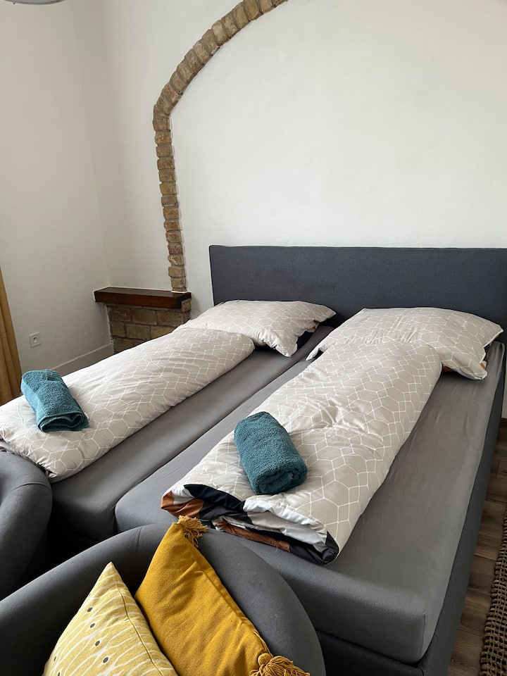 חדר שינה שקט עם מיטת קינג סייז נוחה, ארון בגדים, כורסאות וארון קטן יותר עם נוף לרחוב ולגינה קטנה.