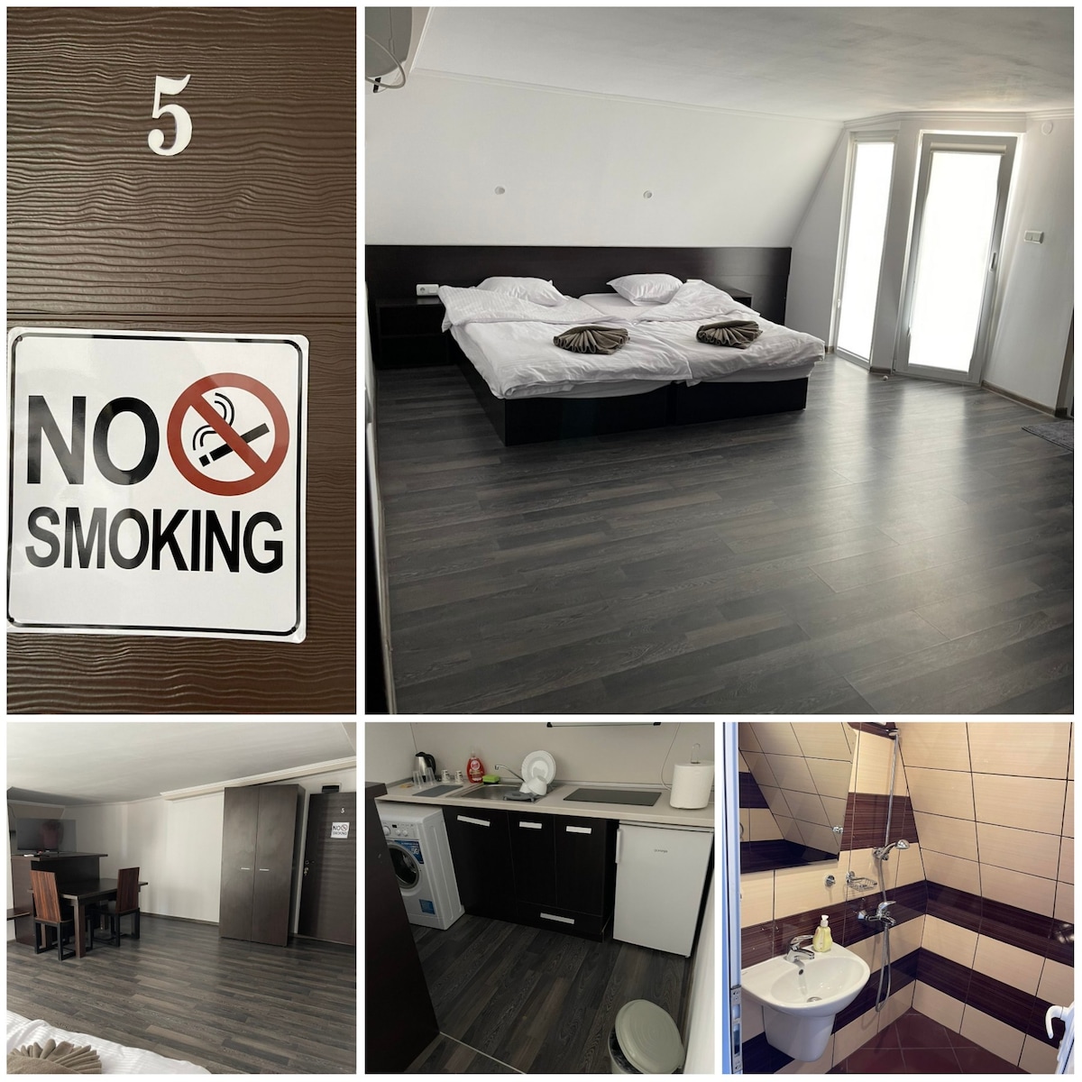 A spacious room features two large beds set against a neutral wall. Bright light enters through glass doors. A dining area with a table and chairs is visible, along with a well-equipped kitchen area. Clean, modern bathroom fixtures are also present.