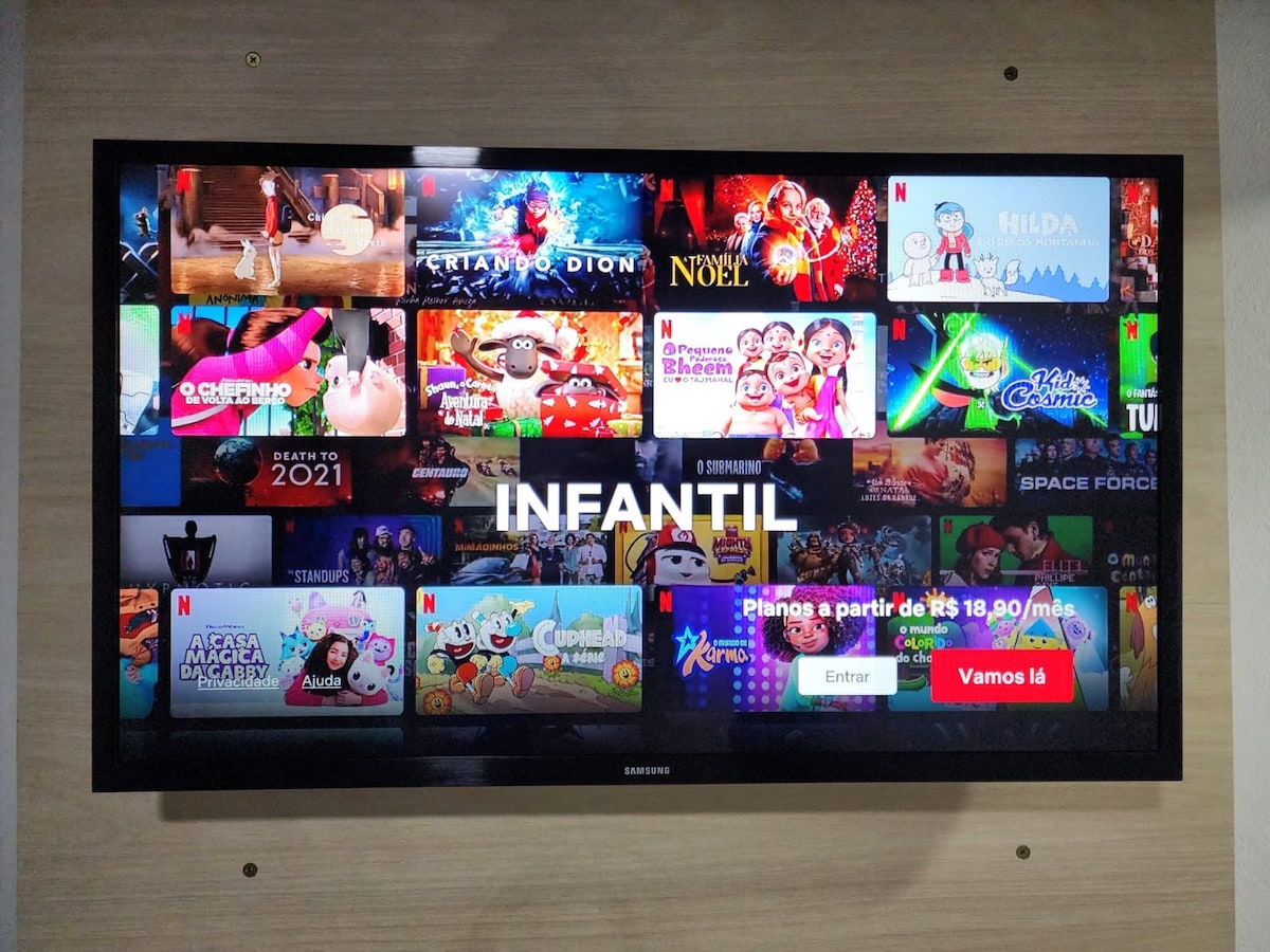 A large flat-screen television displays a variety of animated programs and movies for children. Colorful thumbnails showcase various titles, with a prominent label reading 'INFANTIL' centered on the screen. The interface also features options for navigation and subscription plans along the bottom.