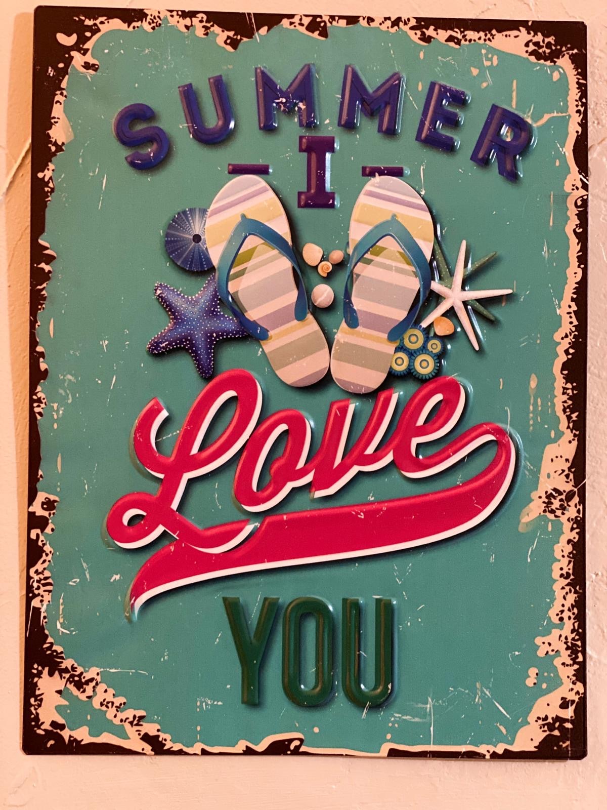 A colorful wall sign features the text 'Summer I Love You' against a turquoise background. Decorative elements include flip-flops, seashells, and starfish, adding to the theme of summer.