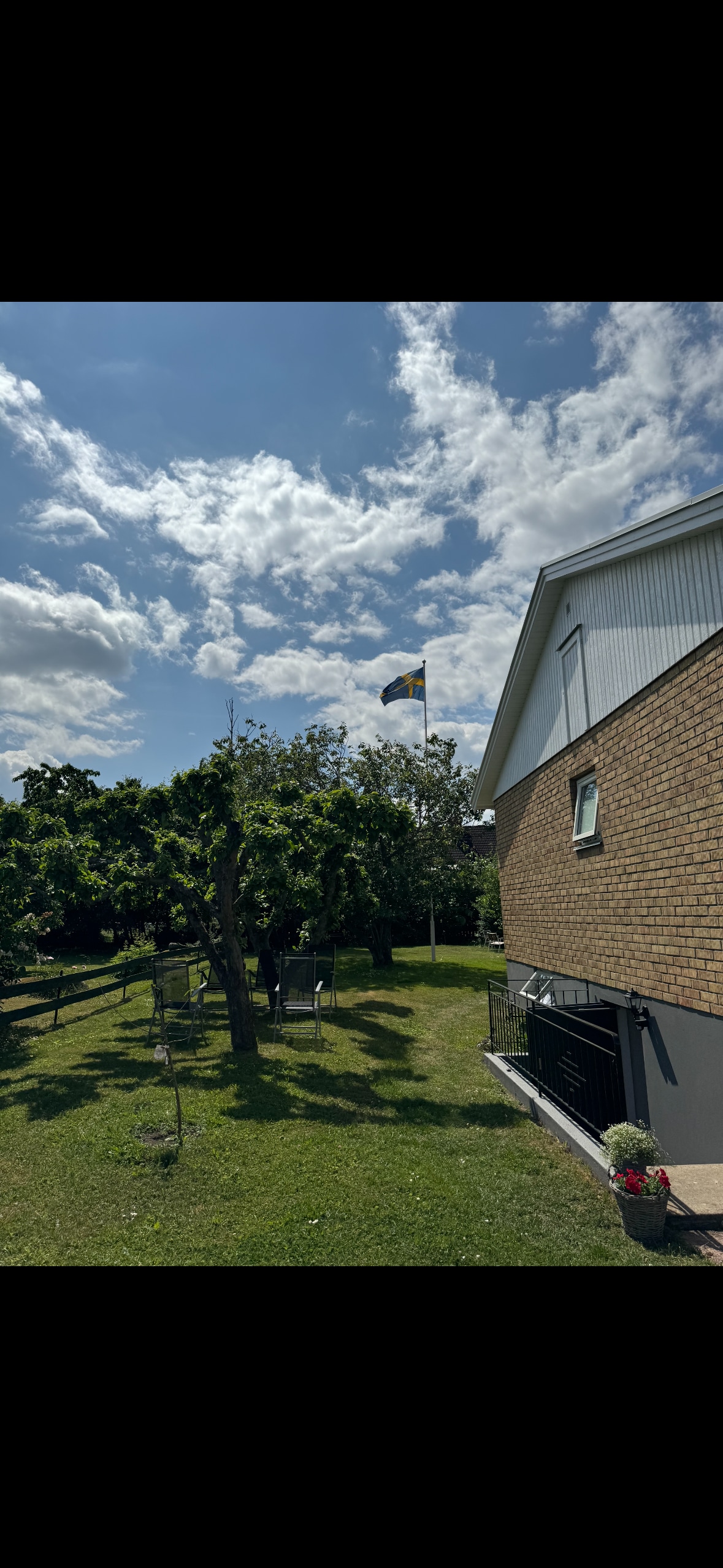 A view of the exterior of a house is shown, featuring a well-maintained lawn with trees and a Ukrainian flag waving against a bright blue sky. The structure displays a combination of brick and siding materials, creating a welcoming appearance.