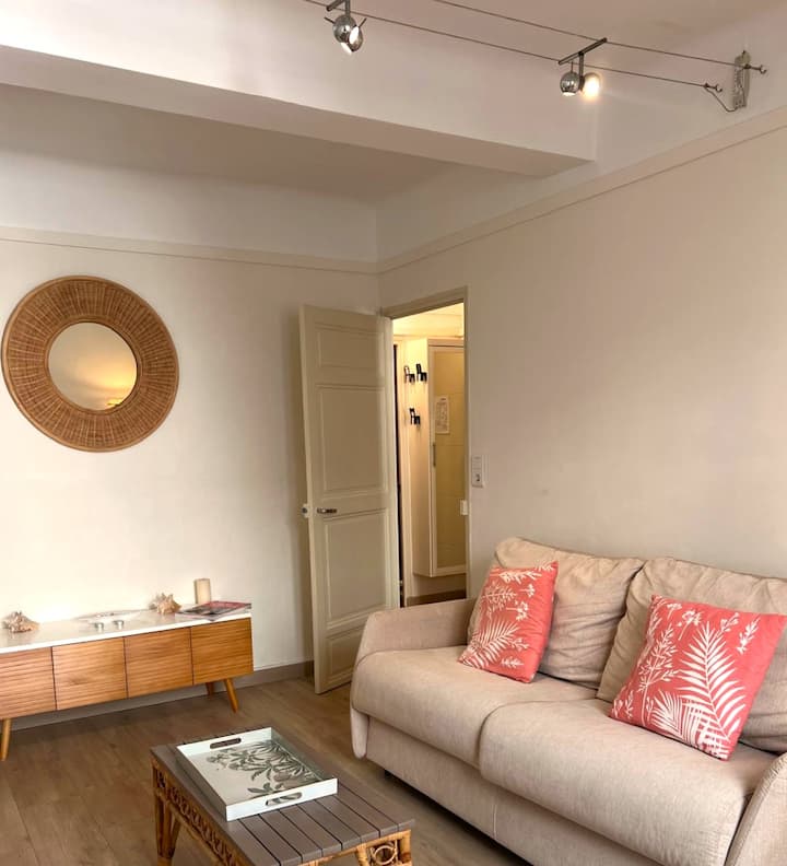 Settle down on the beige sofa: the light from the spotlights and the rattan mirror create a cozy atmosphere, while the coral cushions add a touch of color for a relaxing moment.