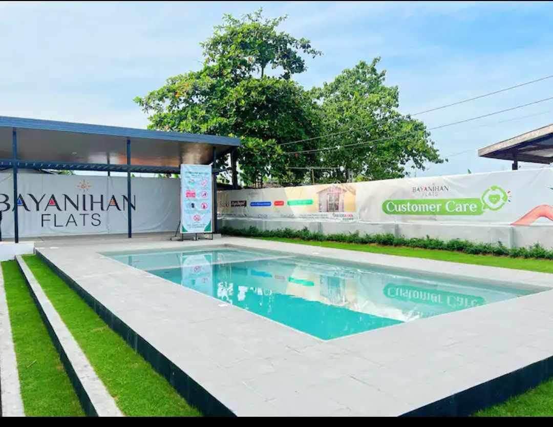 A clean swimming pool is surrounded by neatly trimmed grass, featuring a smooth, tiled deck. A shaded area with a roof provides space for relaxation. Eco-friendly landscaping enhances the outdoor charm, with trees visible in the background and a clear sky above.