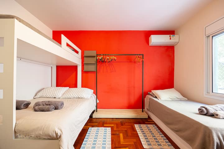 Poschodová posteľ s manželskou posteľou pod ňou, samostatnou posteľou na vrchu a ďalšou samostatnou posteľou vedľa okna a klimatizácie. Zatemnenie okna.