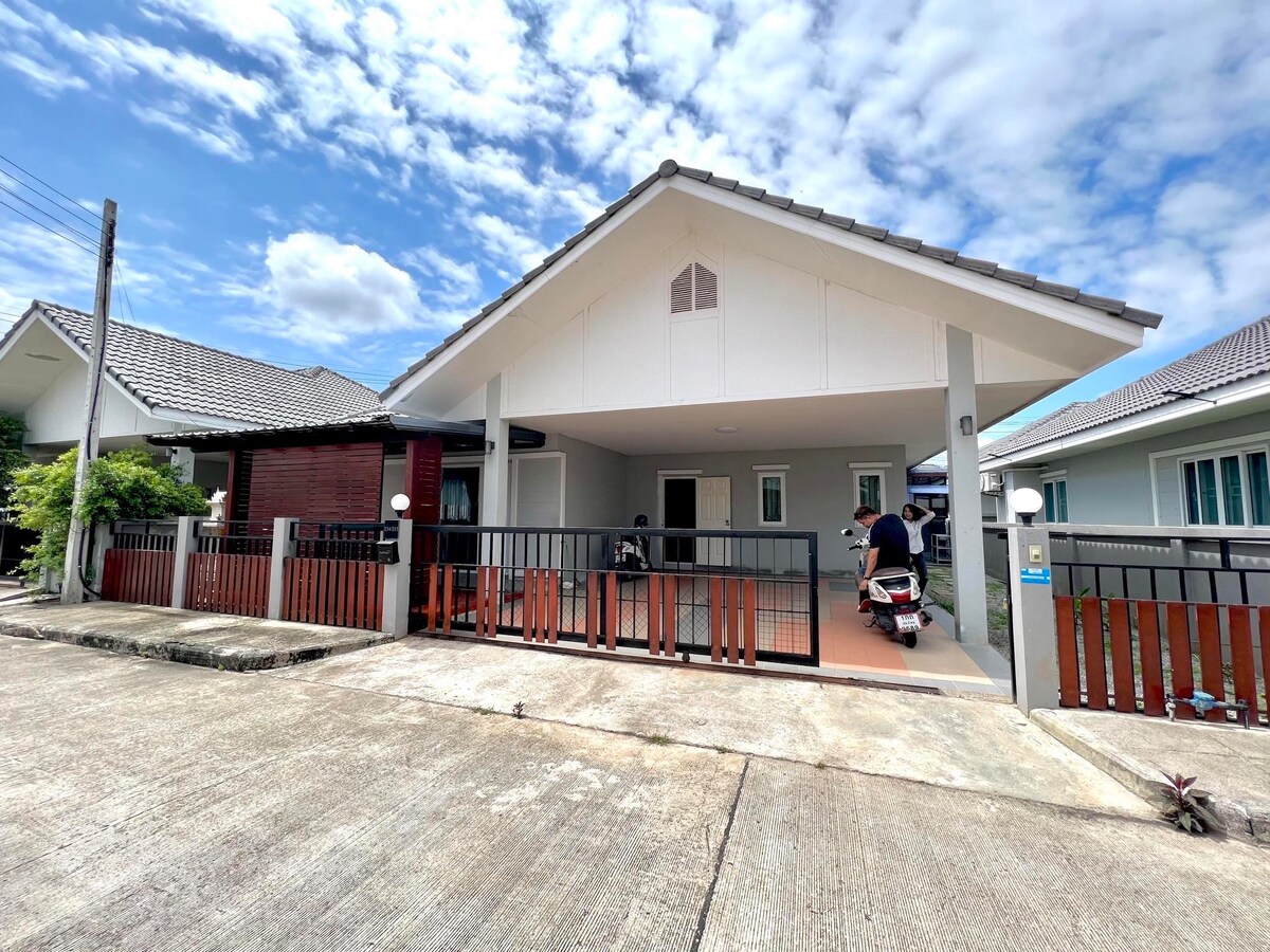 A single-story house is depicted with a sloped roof and an inviting front porch. A smooth driveway leads to the entrance, and a wooden fence outlines the property. The bright sky is visible above, enhancing the overall clarity of the scene.