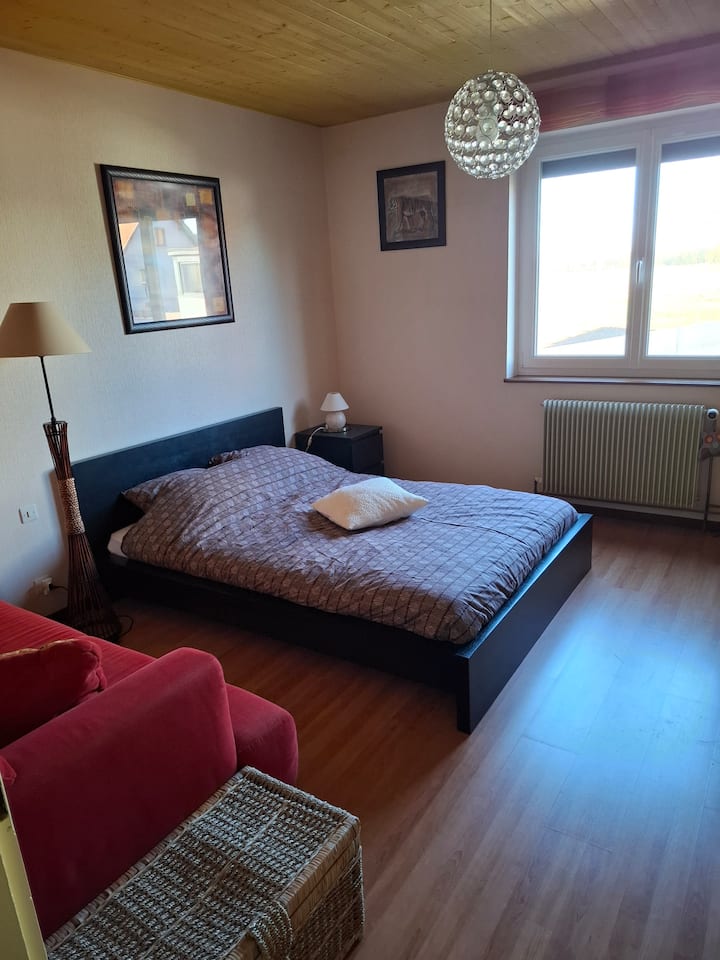 Chambre avec lit 140 X 200cm qui se trouve au même niveau que les pièces de vie. Armoire avec cintres et bureau dans la pièce.