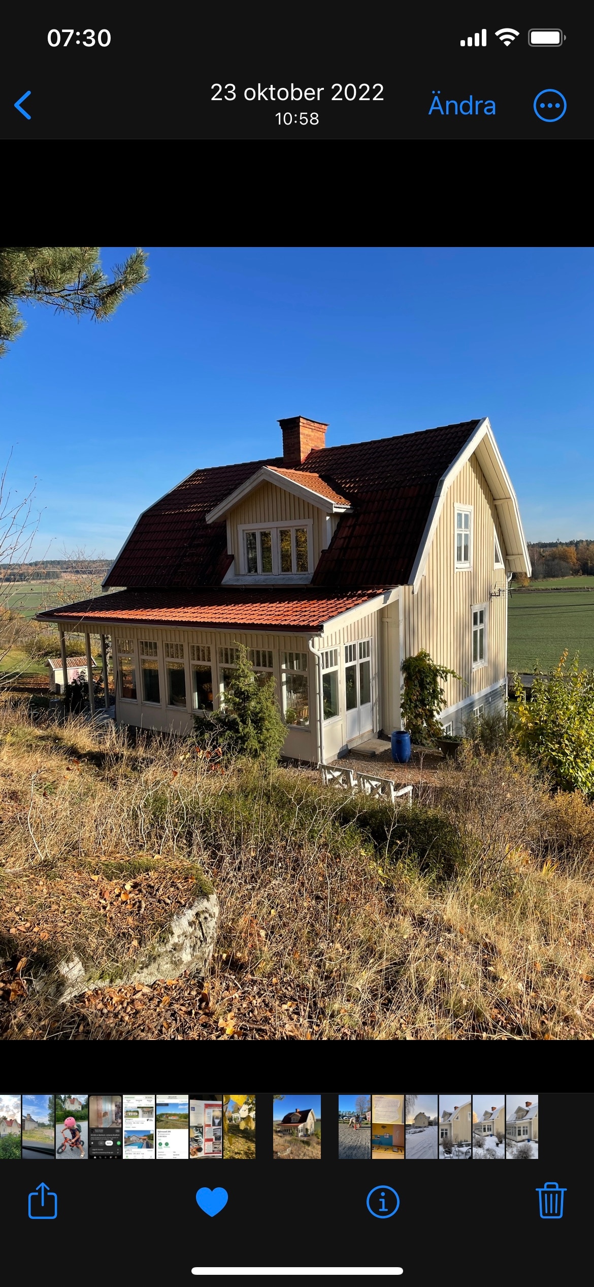 The house features a charming exterior with a sloped roof and welcoming porch. Large windows allow natural light to fill the interior, while a lush green landscape and open fields are visible in the background, contributing to a serene atmosphere.