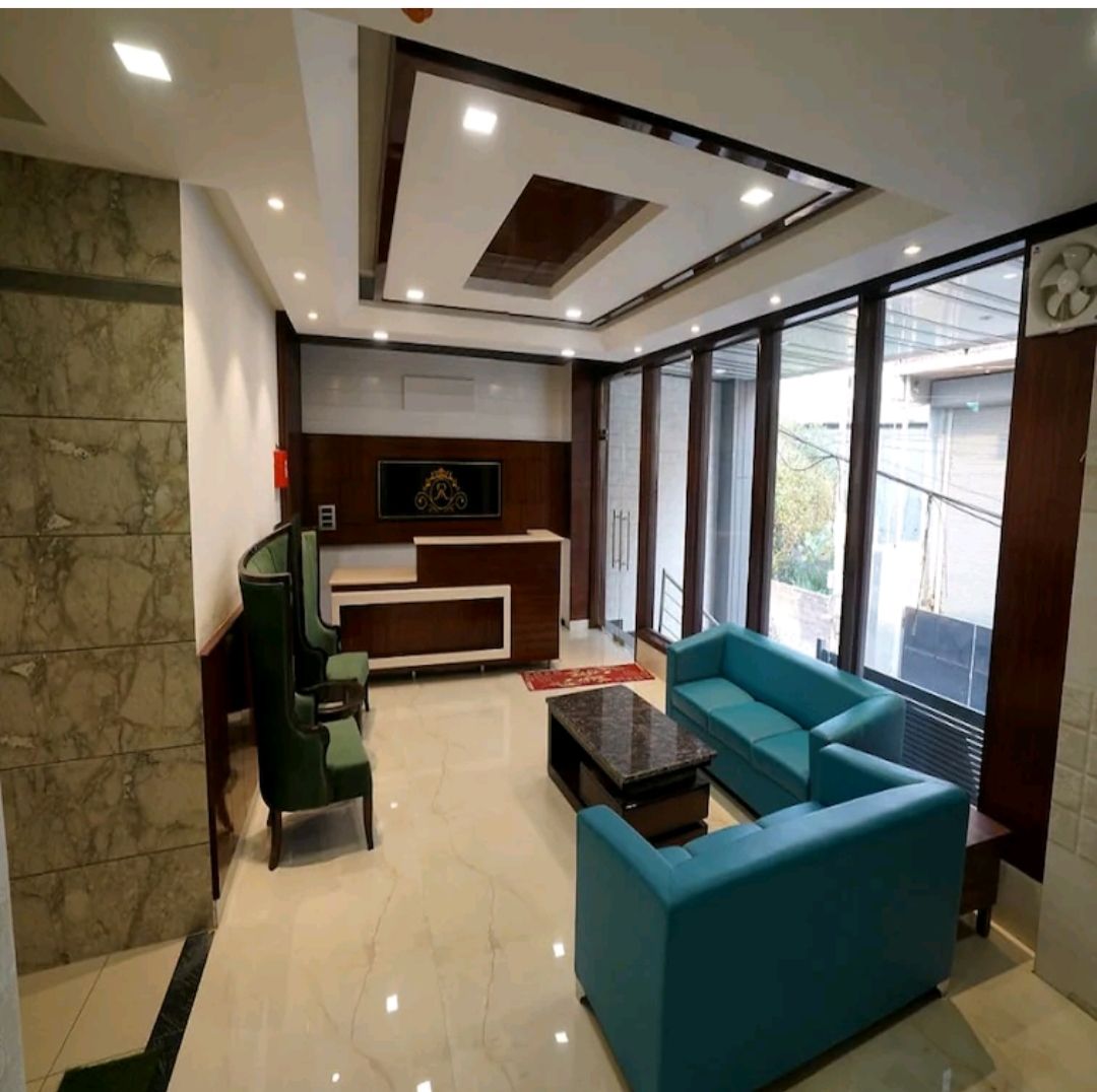 A modern lounge area is characterized by sleek marble flooring and large windows allowing natural light to fill the space. Comfortable teal sofas are arranged around a dark coffee table. A stylish accent wall and decorative elements enhance the contemporary design.