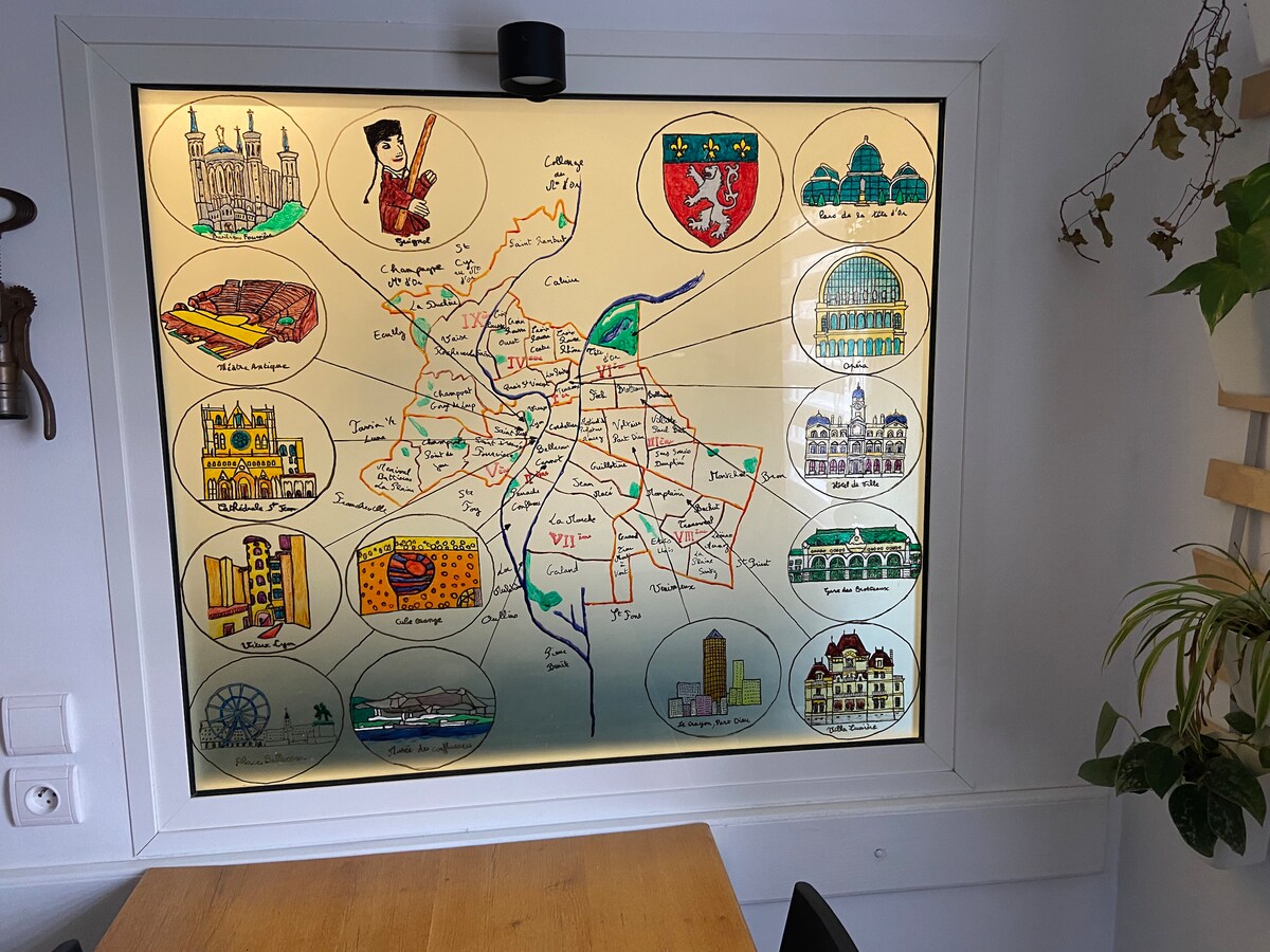 A colorful illustrated map of a city is displayed in a window frame, featuring various landmarks and attractions. The map includes small drawings and labels, providing an educational overview of the area. A wooden table is visible in the foreground.