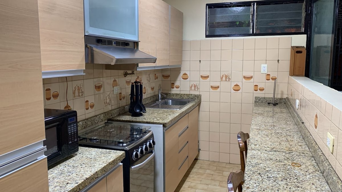 A fully equipped kitchen features wooden cabinetry and granite countertops. Essential appliances, including a microwave and a stove, are present. The design incorporates textured tiles with a light color palette, providing a functional space with ample counter area for meal preparation.